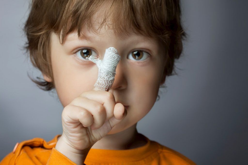 young boy in orange shirt showing pointer finger wrapped in bandage closeup he got at immediate care