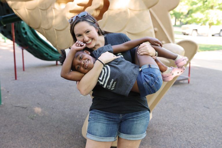 smiling young woman holding smiling, young african american girl at playground