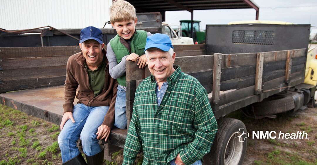 a boy, a middle aged man, and an elderly man all in jeans and flannel shirts sitting on the back of a farm truck